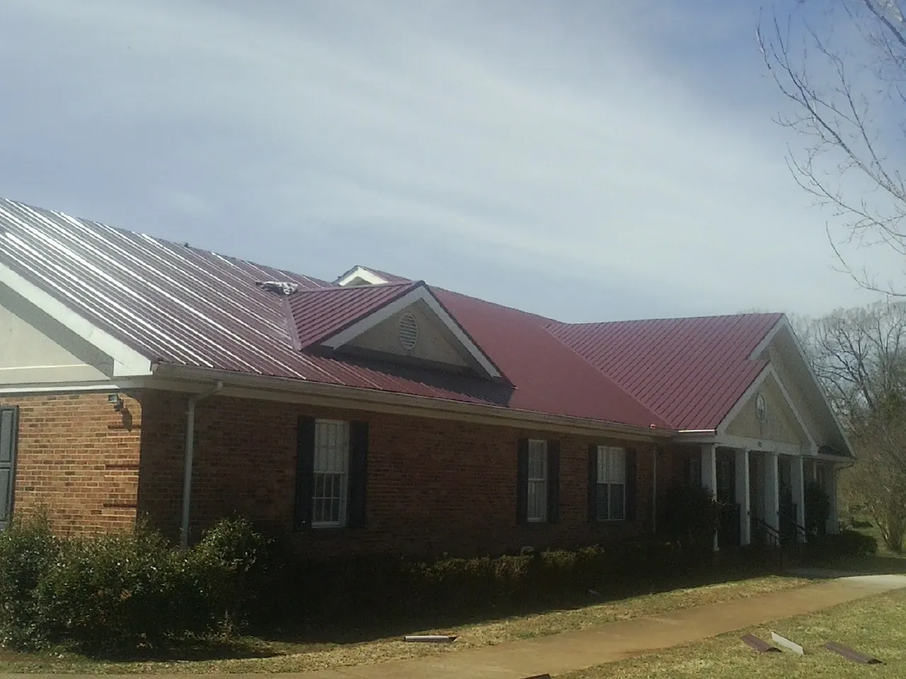 Red metal roof with gabled entries on a long brick building, from a Hail Damage Roof Repair job in Mexico