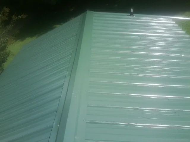 New green metal panels meeting at the ridge of a roof — Flat Roof Repair work by our crew in Mexico